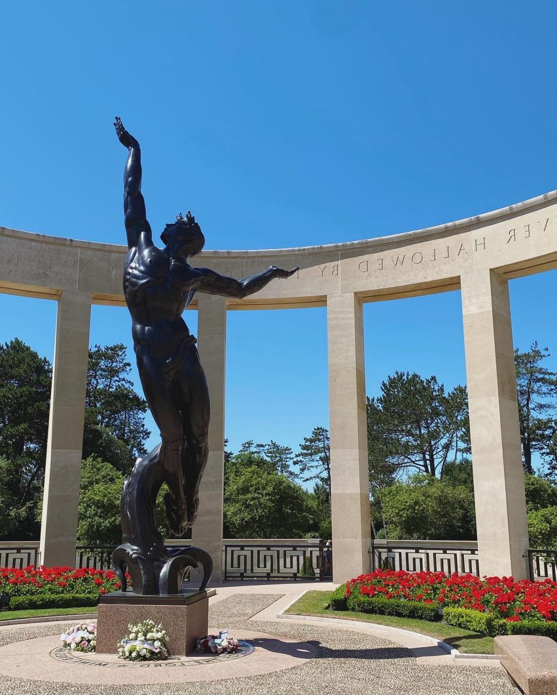 A picture of a male statue in front of a flower bed.