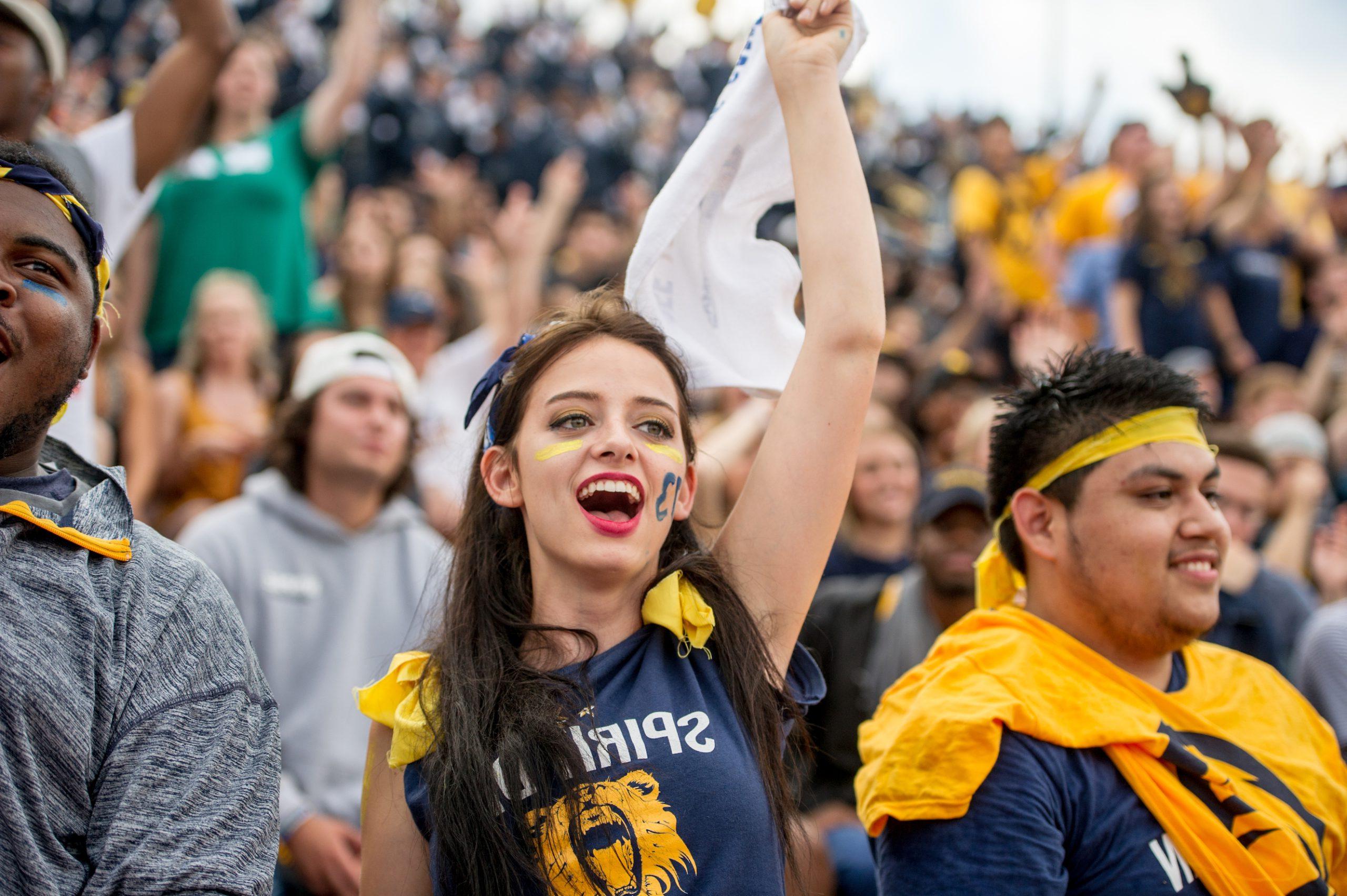 A Female student waving a flag and cheering at the foot ball stadium.