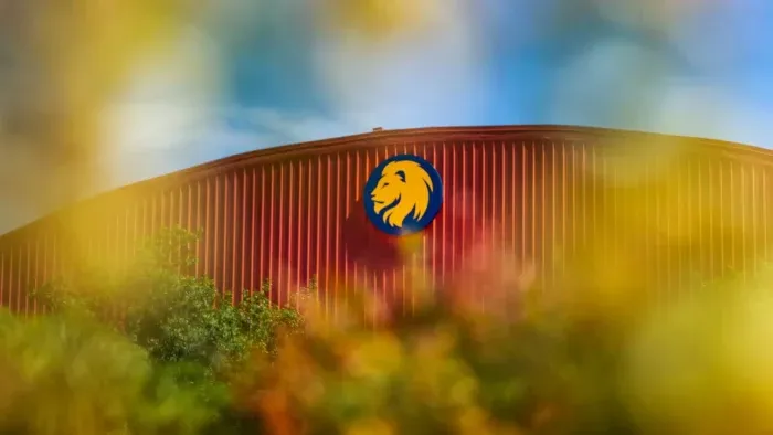 Dome-topped fieldhouse peaks out from behind trees. Lion head logo is placed at the top of the building.